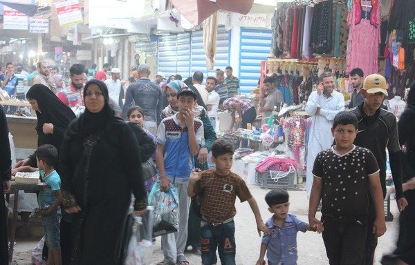 Une mère fait les courses avec ses enfants dans un marché à Ramadi. Les femmes sous le règne de "l'Etat islamique en Irak et au Levant" étaient forcées à couvrir leurs visages avec des niqabs et les hommes devaient faire pousser les barbes. [Saif Ahmed/Diyaruna]