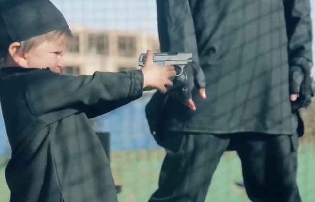 Image tirée d'une vidéo de l'EIIL montrant un activiste donnant une arme à feu à un jeune enfant. Quelques instants plus tard, l'enfant abat un « apostat ».