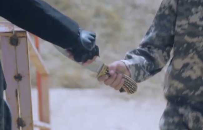 Image tirée d'une vidéo de l'EIIL montrant un activiste donnant un couteau à un jeune garçon. Peu après, le garçon décapite un « apostat ».