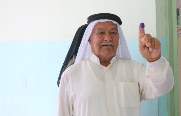 Haj Khamis Abou Ahmed lève le doigt, trempé dans l'encre bleue, pour montrer qu'il a voté au bureau de vote du lycée al-Jamhouriya. [Saif Ahmed/Diyaruna]