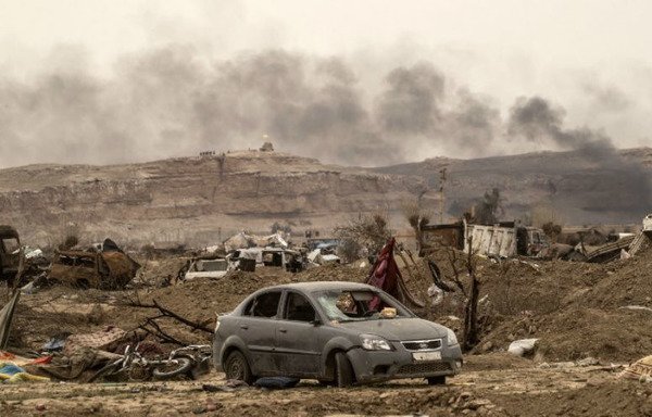 Cette photo prise le 24 mars montre de la fumée s'élevant derrière des véhicules détruits et des bâtiments endommagés dans le village d'al-Baghouz, un jour après que l'EIIS a perdu son dernier territoire en Syrie. [Delil Souleiman/AFP]
