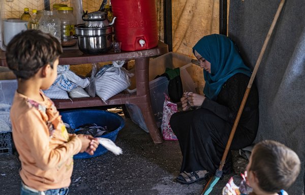 Alaa Souleiman al-Saleh, une bénévole s'occupant de 24 orphelins qui seraient liés à des combattants étrangers de l'EIIS, tricote un vêtement sous le regard d'enfants dans un camp à Aïn Issa. [Delil Souleiman/AFP]