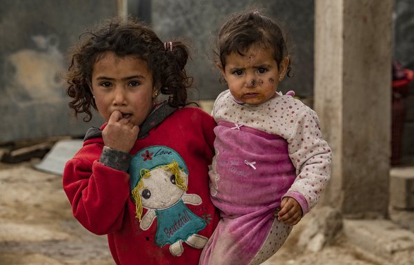 Une fillette porte sa sœur qui souffre de leishmaniose, une maladie de la peau provoquée par un parasite microscopique propagé par le phlébotome, dans le village d'al-Baghouz, dans l'est de la Syrie, le 13 mars. [Delil Souleiman/AFP]