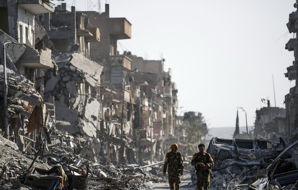 Fighters of the Syrian Democratic Forces (SDF) walk down a street in al-Raqa past destroyed vehicles and heavily damaged buildings on October 20, 2017, after a Kurdish-led force expelled ISIS from the northern Syrian city, formerly their 'capital'. [Bulent Kilic/AFP]