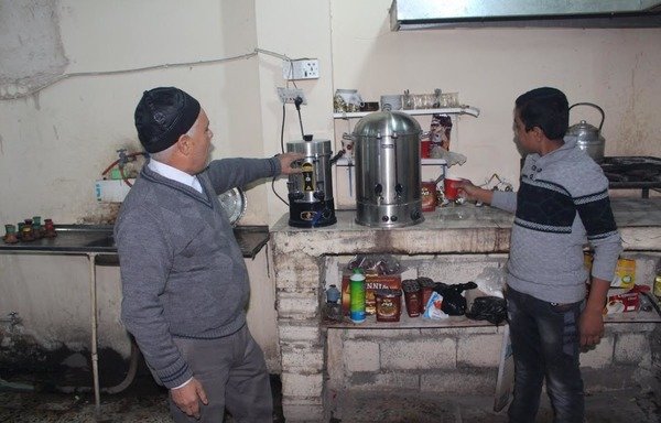Abu Raed al-Halboosi (left), owner of Samir Amis shisha and coffee shop in Fallujah, rehabilitated his shop after it sustained heavy damage during ISIL's rule, and is now serving his customers once more coffee, tea and shisha. [Saif Ahmed/Diyaruna]