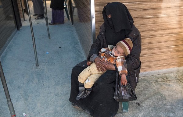 امرأة سورية نازحة تحمل طفلًا أثناء الانتظار خارج عيادة مؤقتة في مخيم الهول للاجئين بمحافظة الحسكة السورية يوم 7 شباط/فبراير. [فاضل سينا/وكالة الصحافة الفرنسية]