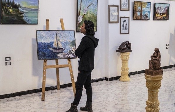 Amal al-Attar, a 37-year-old Syrian artist, looks at her artworks on display during an exhibition at the first cultural centre to open since ISIS's rule ended in the eastern Syrian city of al-Raqa, on May 1st, 2019. [Delil Souleiman/AFP]