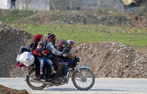 Displaced Syrians ride a motorcycle as they arrive to Deir al-Ballut camp in Afrin's countryside along the border with Turkey, on February 19th. [Rami al-Sayed/AFP]