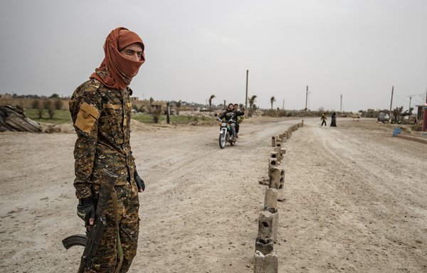 A fighter of the Syrian Democratic forces stands guard at the entrance of the eastern Syrian village of al-Baghouz on March 13th, a year after the fall of ISIS. [Delil Souleiman/AFP]