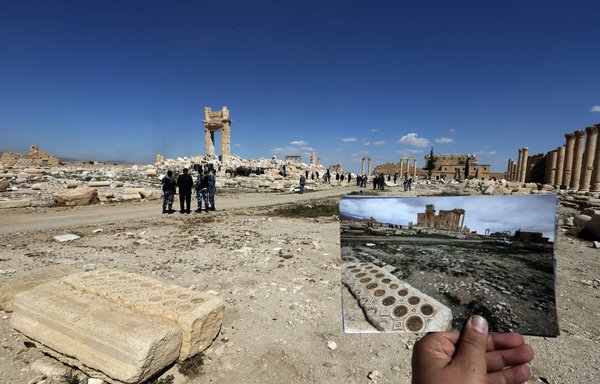 صورة التقطت في 31 آذار/مارس 2016 لمصور يحمل صورة التقطها لمعبد بل في تدمر يوم 14 آذار/مارس 2014، وهو يقف أمام أنقاض المعبد التاريخي بعد أن دمره تنظيم داعش في أيلول/سبتمبر 2015. [جوزيف عيد/وكالة الصحافة الفرنسية]