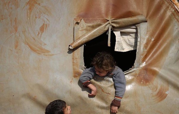 در اردوگاه آوارگان، یک کودک سوری از داخل چادر با کودکی دیگر صحبت می‌کند. [علی حاج سلیمان]